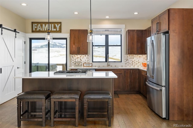 kitchen with a barn door, a sink, light countertops, tasteful backsplash, and stainless steel fridge