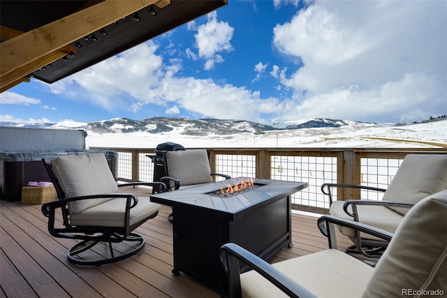 snow covered deck featuring a mountain view and a fire pit