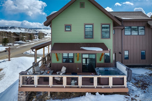 snow covered back of property featuring a deck, a shingled roof, and board and batten siding