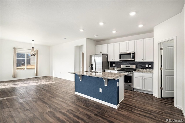 kitchen featuring appliances with stainless steel finishes, white cabinets, a kitchen breakfast bar, light stone counters, and a center island with sink