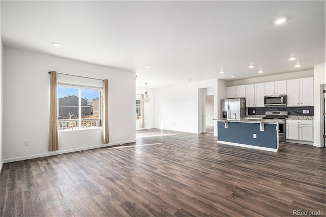 kitchen with a kitchen island with sink, stainless steel appliances, white cabinets, a kitchen bar, and dark hardwood / wood-style flooring