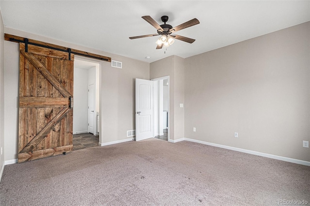 unfurnished bedroom featuring dark carpet, a barn door, and ceiling fan