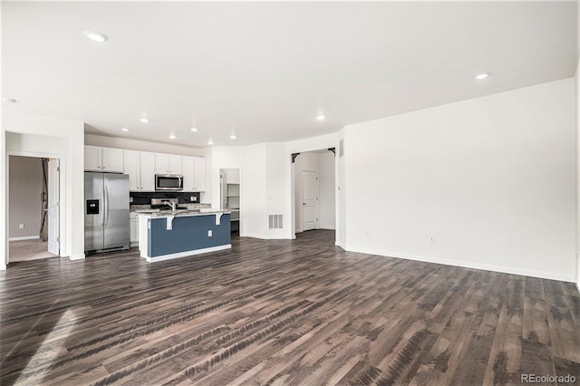 kitchen with a breakfast bar area, appliances with stainless steel finishes, a kitchen island with sink, white cabinetry, and dark hardwood / wood-style floors