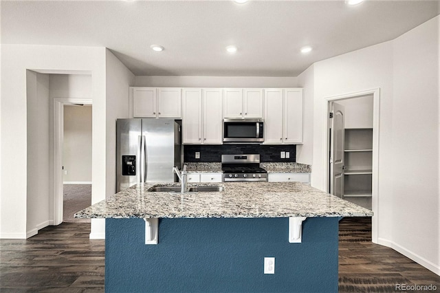 kitchen featuring white cabinetry, light stone counters, a center island with sink, and appliances with stainless steel finishes