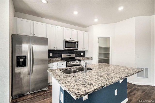 kitchen with sink, appliances with stainless steel finishes, light stone countertops, an island with sink, and white cabinets