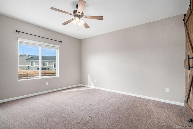 carpeted empty room featuring a barn door and ceiling fan