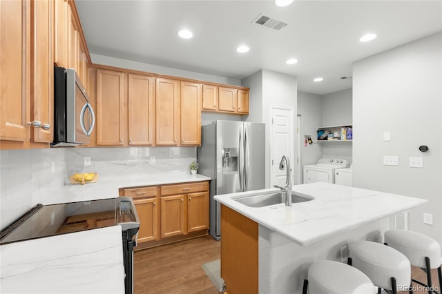 12973 Grant Cir E Unit A, Thornton, CO 80241 - kitchen featuring appliances with stainless steel finishes, washing machine and clothes dryer, a sink, light wood-type flooring, and a kitchen bar