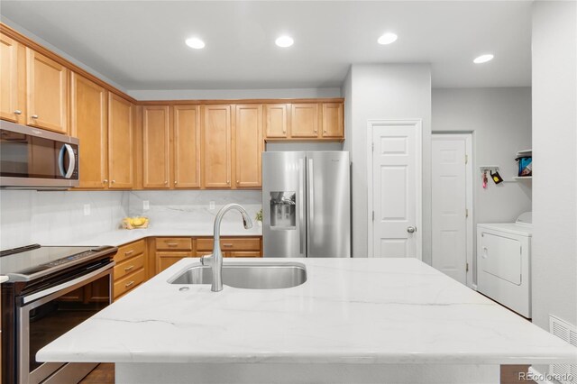 12973 Grant Cir E Unit A, Thornton, CO 80241 - kitchen featuring appliances with stainless steel finishes, a sink, a kitchen island with sink, light stone countertops, and washing machine and dryer