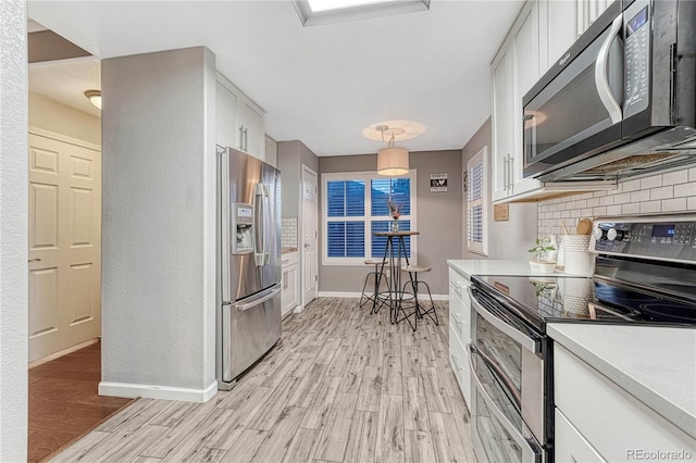 kitchen with appliances with stainless steel finishes, light wood-type flooring, white cabinetry, and decorative backsplash