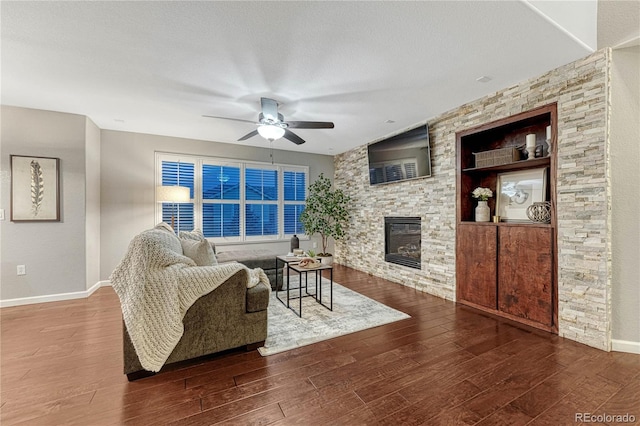 living room with built in shelves, a stone fireplace, a textured ceiling, wood finished floors, and baseboards