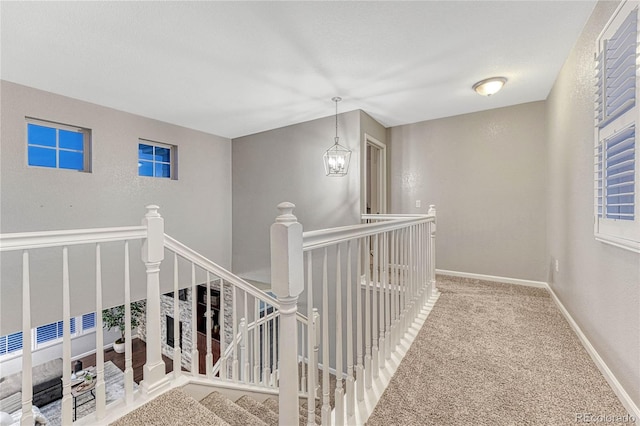 hall with carpet floors, baseboards, an upstairs landing, and an inviting chandelier