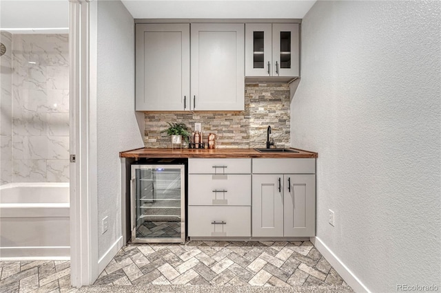 bar with backsplash, a sink, wet bar, beverage cooler, and baseboards