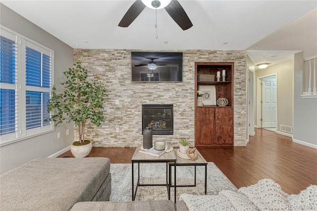 living area featuring built in shelves, wood finished floors, visible vents, baseboards, and a glass covered fireplace