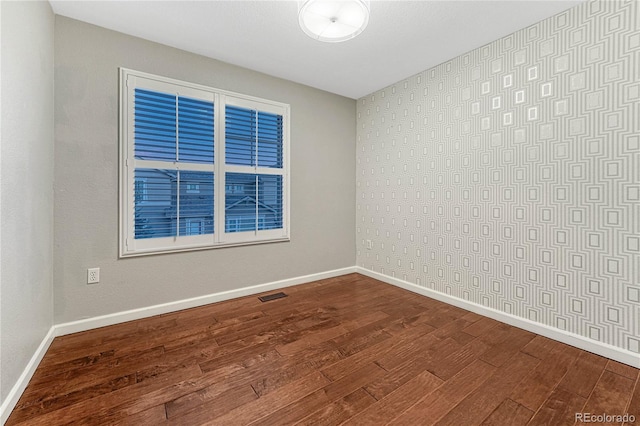 spare room with dark wood-style floors, visible vents, and baseboards