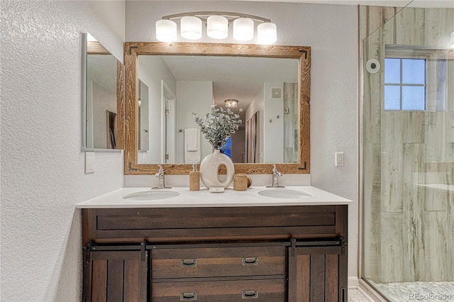 full bath with a textured wall, double vanity, a sink, and a shower with shower door