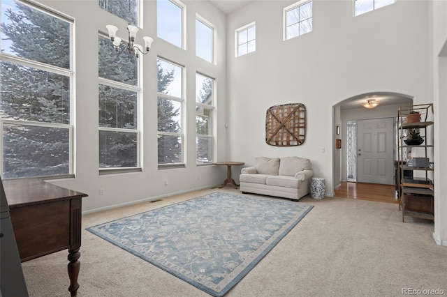 carpeted living room featuring a towering ceiling, an inviting chandelier, and plenty of natural light