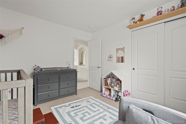 bedroom with a closet, a nursery area, and light colored carpet