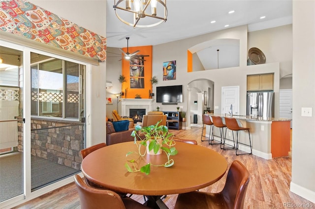 dining room with ceiling fan with notable chandelier, a high ceiling, and light hardwood / wood-style floors