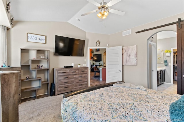 bedroom with ensuite bath, lofted ceiling, light colored carpet, a barn door, and ceiling fan