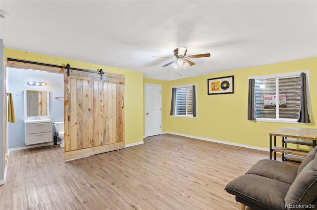 sitting room with ceiling fan, a barn door, and light hardwood / wood-style flooring