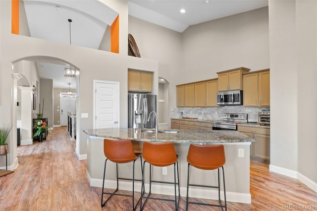 kitchen featuring stainless steel appliances, sink, an island with sink, backsplash, and high vaulted ceiling