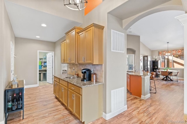 kitchen featuring sink, a kitchen bar, pendant lighting, and light stone countertops