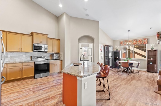 kitchen with sink, light stone counters, backsplash, a kitchen island with sink, and appliances with stainless steel finishes