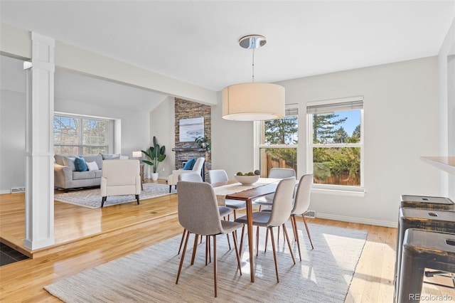 dining area featuring lofted ceiling with beams, wood-type flooring, a healthy amount of sunlight, and a fireplace