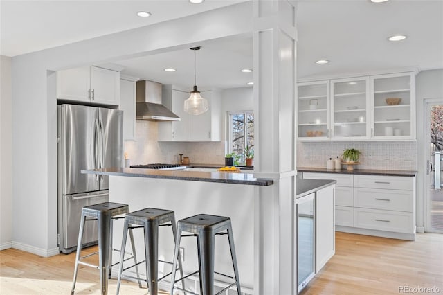 kitchen with wall chimney exhaust hood, white cabinetry, appliances with stainless steel finishes, a kitchen breakfast bar, and pendant lighting