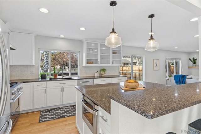 kitchen featuring pendant lighting, white cabinetry, sink, dark stone counters, and light wood-type flooring