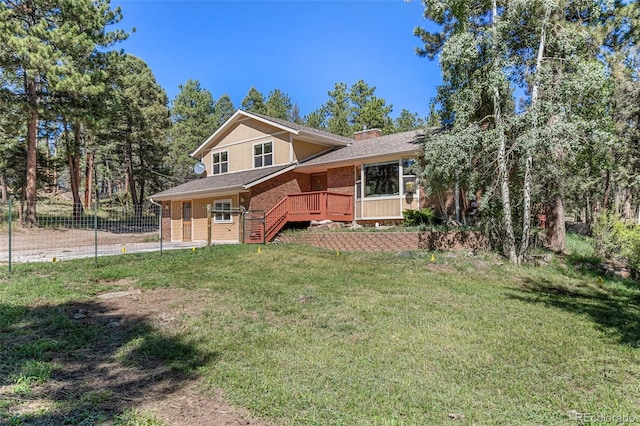 tri-level home with brick siding, fence, a wooden deck, a front lawn, and a chimney