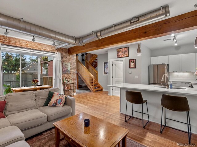 2524 Champa St Unit 1, Denver, CO 80205 - living room featuring light wood-style floors, track lighting, stairway, brick wall, and beam ceiling