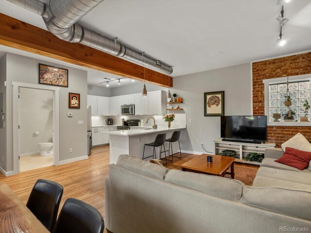 2524 Champa St Unit 1, Denver, CO 80205 - living room with rail lighting, brick wall, baseboards, and light wood-style flooring