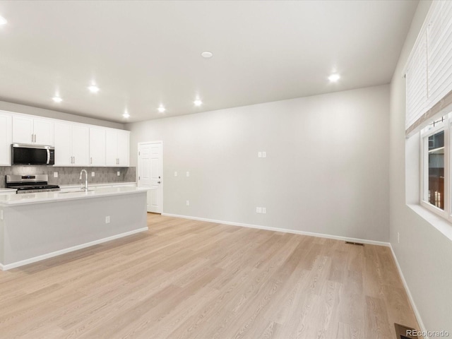 kitchen featuring sink, light hardwood / wood-style flooring, white cabinets, stainless steel appliances, and backsplash