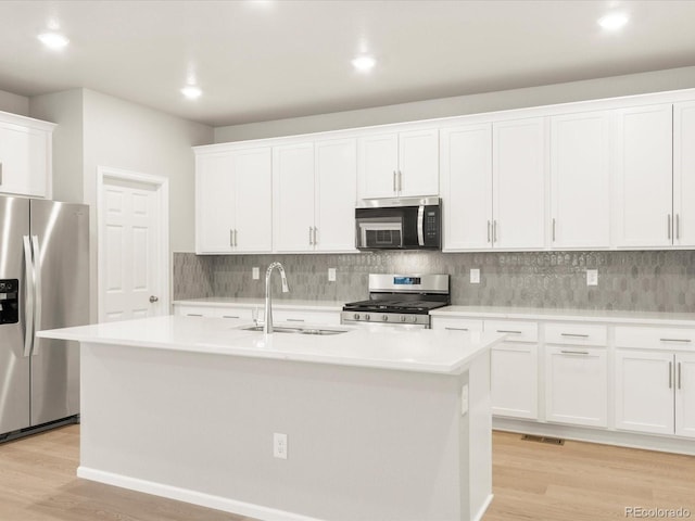 kitchen featuring appliances with stainless steel finishes, white cabinetry, an island with sink, sink, and decorative backsplash