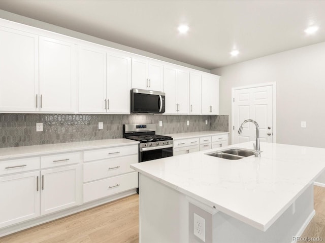 kitchen with an island with sink, white cabinetry, sink, light stone counters, and stainless steel appliances