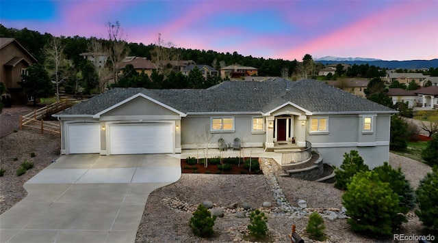ranch-style home with driveway, an attached garage, stucco siding, and roof with shingles