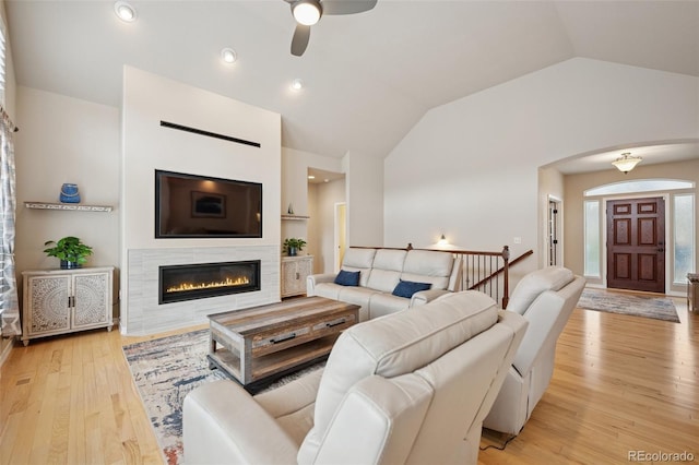 living area with arched walkways, lofted ceiling, ceiling fan, light wood finished floors, and a glass covered fireplace