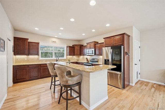 kitchen with appliances with stainless steel finishes, light wood-style flooring, a center island, decorative backsplash, and recessed lighting