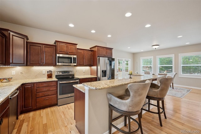 kitchen featuring appliances with stainless steel finishes, light wood finished floors, a kitchen bar, tasteful backsplash, and a kitchen island