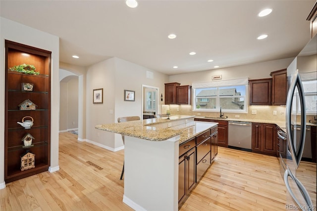 kitchen with stainless steel appliances, arched walkways, light wood-type flooring, backsplash, and recessed lighting