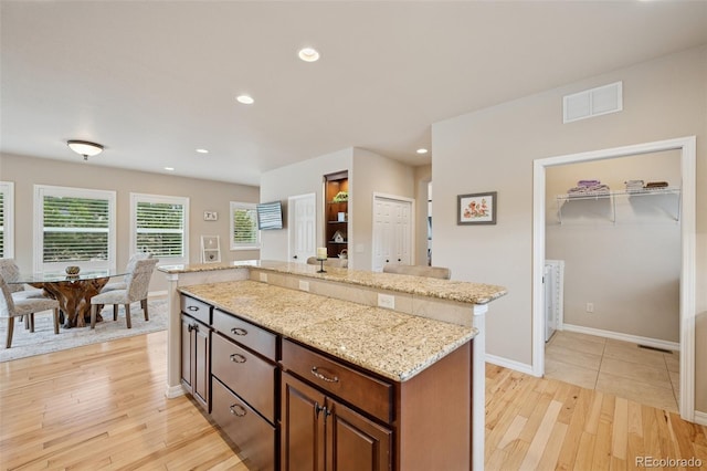 kitchen with light wood finished floors, light stone counters, recessed lighting, a kitchen island, and baseboards