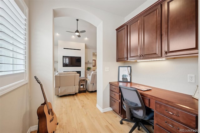 home office with ceiling fan, light wood finished floors, baseboards, and built in study area