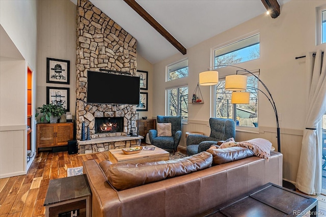 living room with hardwood / wood-style flooring, beam ceiling, high vaulted ceiling, and a stone fireplace