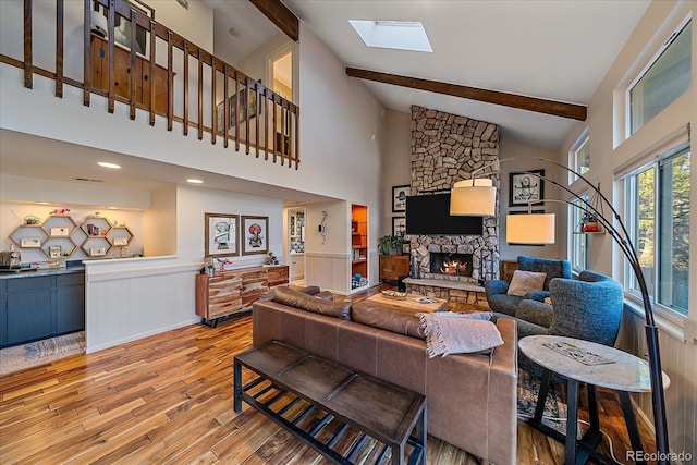 living room with a skylight, high vaulted ceiling, beamed ceiling, a fireplace, and light hardwood / wood-style floors