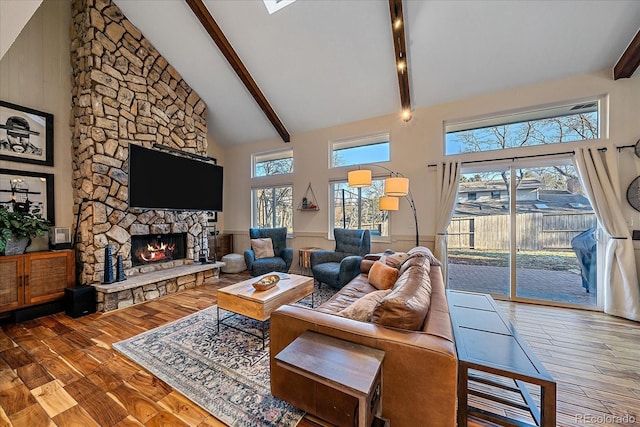 living room with hardwood / wood-style flooring, a stone fireplace, high vaulted ceiling, and beamed ceiling