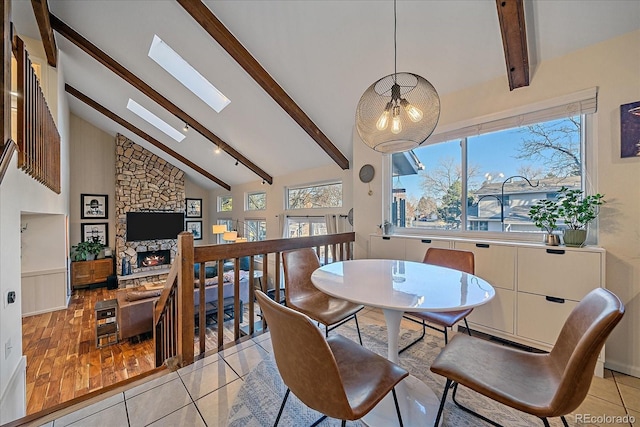 tiled dining area with a stone fireplace, a skylight, high vaulted ceiling, and beamed ceiling