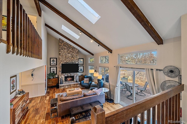 living room featuring hardwood / wood-style floors, beam ceiling, a skylight, high vaulted ceiling, and a stone fireplace