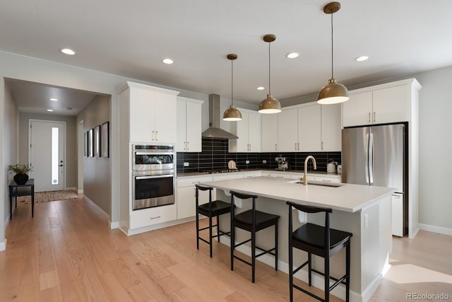 kitchen with sink, white cabinets, stainless steel appliances, a center island with sink, and wall chimney exhaust hood