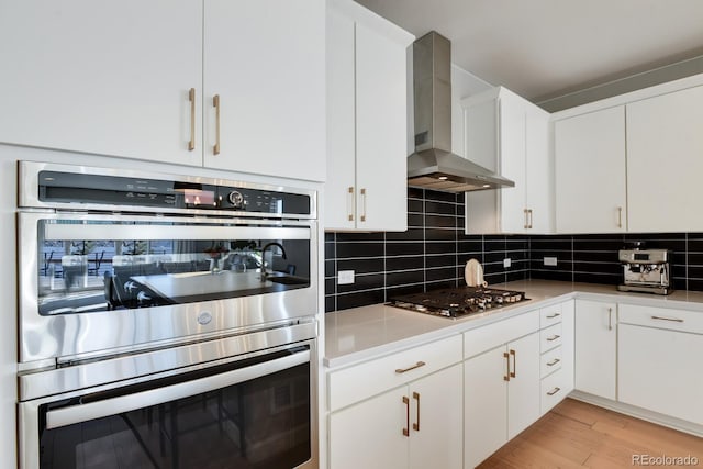 kitchen featuring wall chimney range hood, stainless steel appliances, and white cabinets